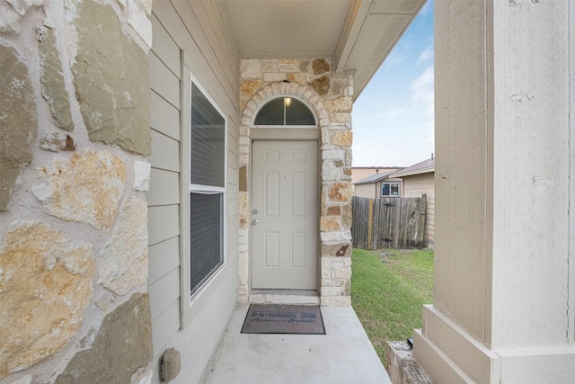 doorway to property featuring stone siding and fence