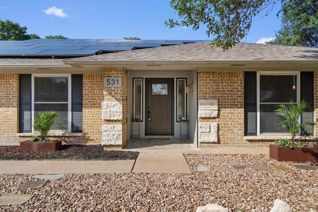 531 Dennis Dr, Round Rock, TX 78664 - doorway to property featuring brick siding, solar panels, and a shingled roof