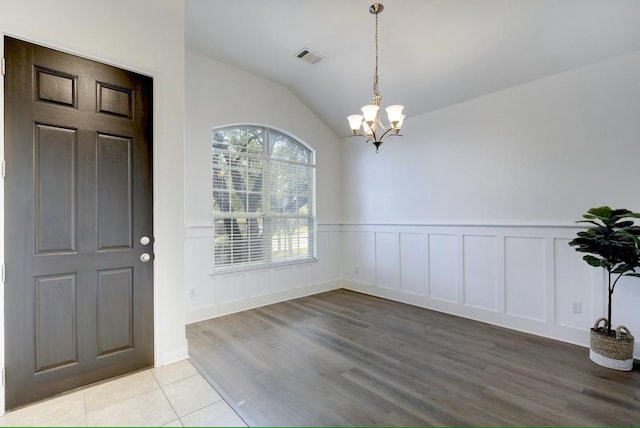 foyer featuring a chandelier, wainscoting, vaulted ceiling, light wood finished floors, and a decorative wall