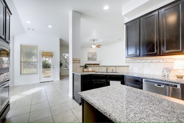kitchen with appliances with stainless steel finishes, a sink, light stone countertops, backsplash, and a ceiling fan