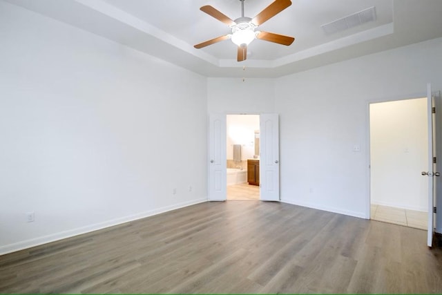 spare room with a raised ceiling, a ceiling fan, wood finished floors, and baseboards