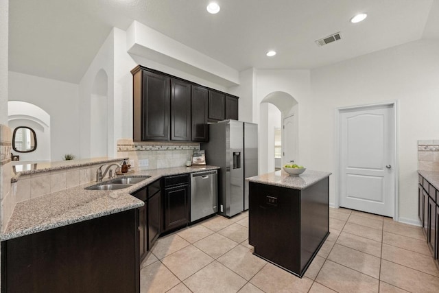 4924 Pyrenees Pass, Bee Cave, TX 78738 - kitchen featuring appliances with stainless steel finishes, arched walkways, tasteful backsplash, light stone countertops, and a kitchen island
