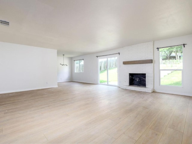 unfurnished living room with light wood-style floors, a fireplace, baseboards, and a chandelier