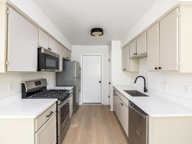 kitchen featuring stainless steel appliances, a sink, light wood-type flooring, and light countertops