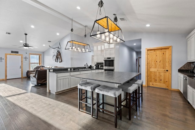 kitchen with lofted ceiling, dark countertops, white cabinets, a center island, and recessed lighting