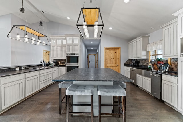 kitchen featuring lofted ceiling, stainless steel appliances, dark countertops, a breakfast bar, and a sink