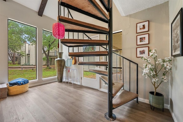staircase with healthy amount of natural light, wood finished floors, baseboards, and beamed ceiling