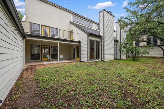 back of property with a balcony, a patio area, a yard, a chimney, and stucco siding