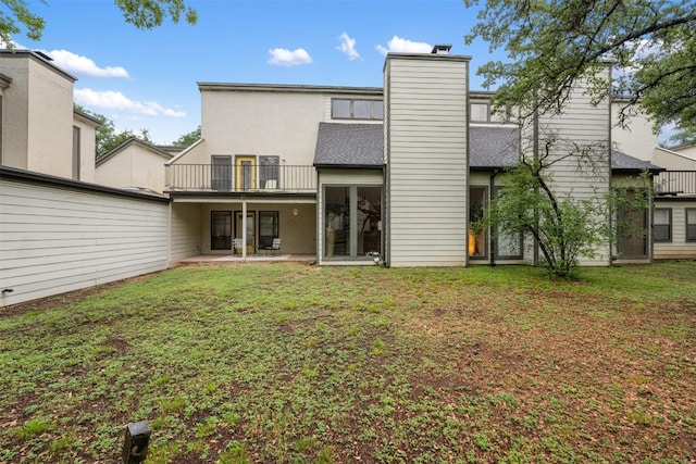 back of property featuring a balcony, a yard, and a chimney