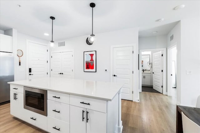 3101 Govalle Ave Unit 114, Austin, TX 78702 - kitchen with built in appliances, white cabinets, light wood-style floors, hanging light fixtures, and recessed lighting