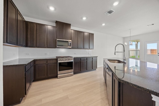 3747 Liberi Ln, Round Rock, TX 78665 - kitchen featuring appliances with stainless steel finishes, dark stone counters, dark brown cabinets, tasteful backsplash, and light wood-type flooring