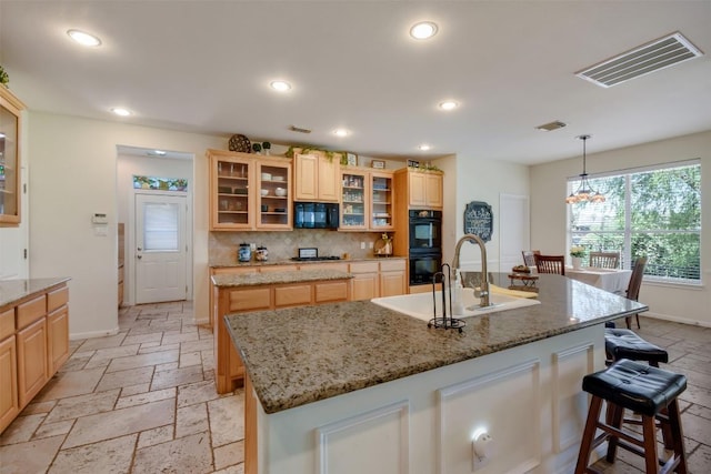 kitchen featuring black appliances, stone tile floors, a kitchen island with sink, a breakfast bar, and recessed lighting