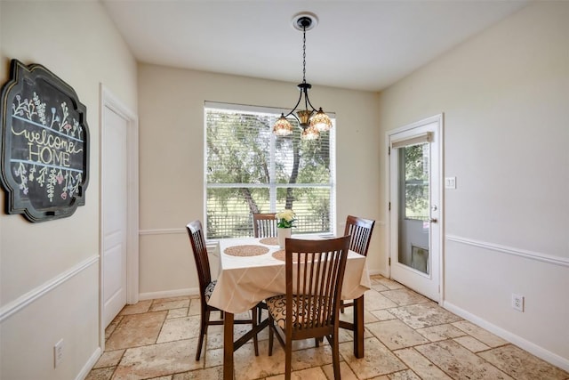 dining space featuring stone tile flooring, a chandelier, and baseboards