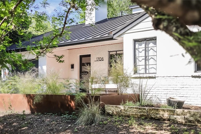 view of front of house with a standing seam roof, metal roof, a chimney, and stucco siding