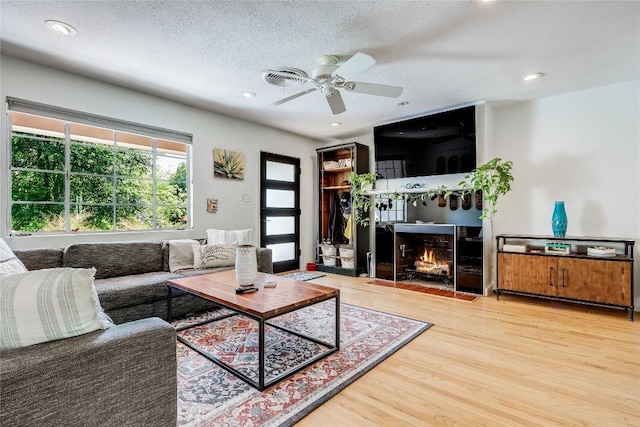 living area featuring wood finished floors, ceiling fan, a textured ceiling, recessed lighting, and a fireplace with flush hearth