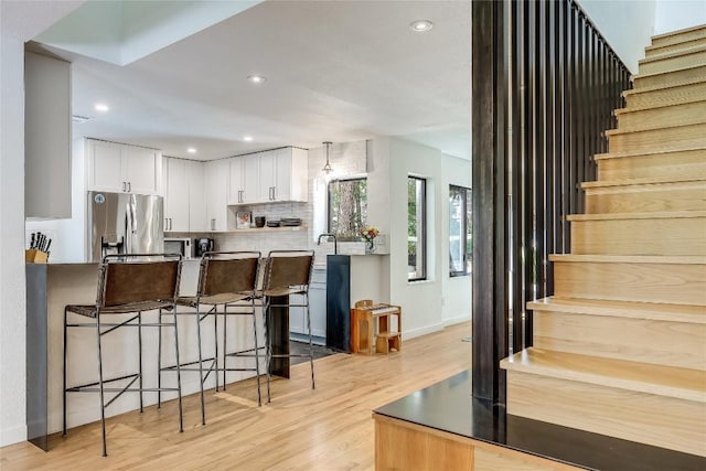 kitchen with stainless steel fridge with ice dispenser, light wood-type flooring, white cabinetry, baseboards, and decorative backsplash