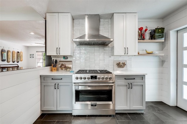 kitchen with wall chimney range hood, high end stainless steel range, light countertops, open shelves, and a textured ceiling
