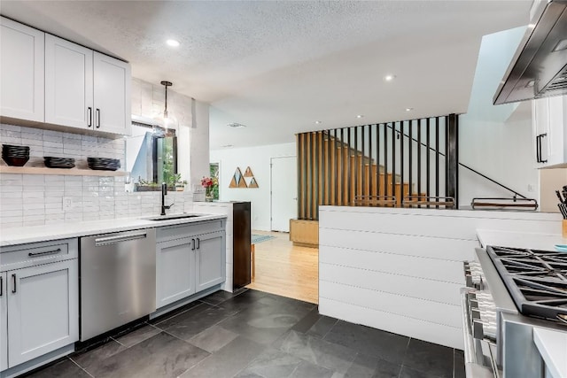 kitchen with appliances with stainless steel finishes, a sink, wall chimney exhaust hood, light countertops, and tasteful backsplash
