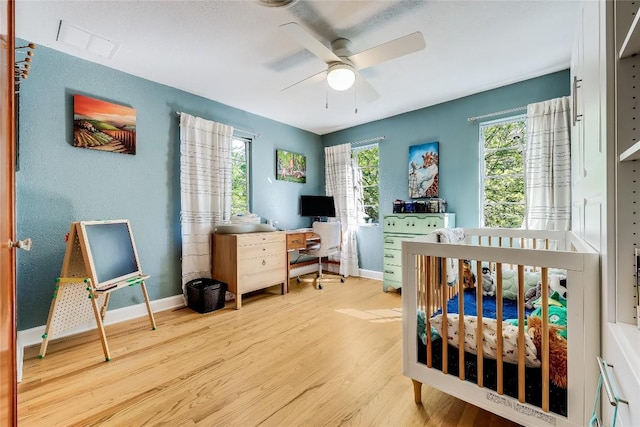 bedroom with wood finished floors, a crib, baseboards, and a ceiling fan