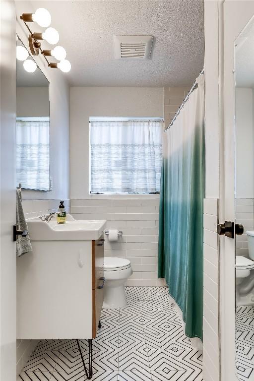 bathroom featuring toilet, tile walls, vanity, a textured ceiling, and a shower with curtain