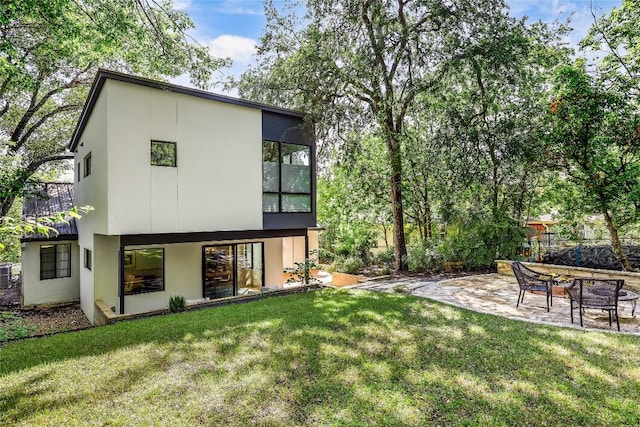 back of house with stucco siding, a patio, and a yard