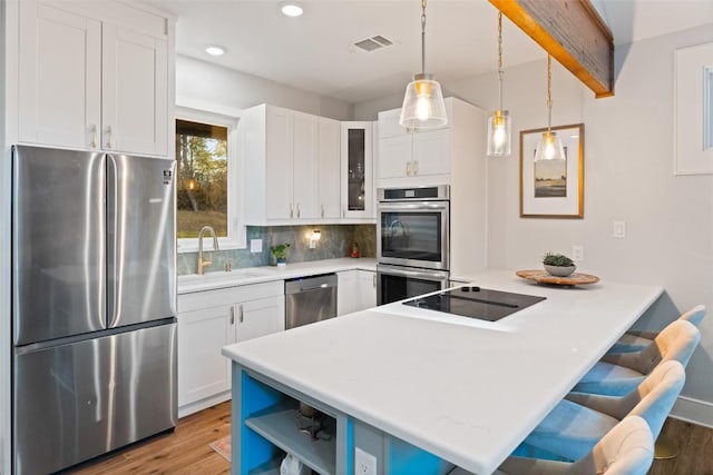 146 Caldwell Ranch Rd, Cedar Creek, TX 78612 - kitchen with appliances with stainless steel finishes, a peninsula, light wood-style floors, a kitchen bar, and recessed lighting