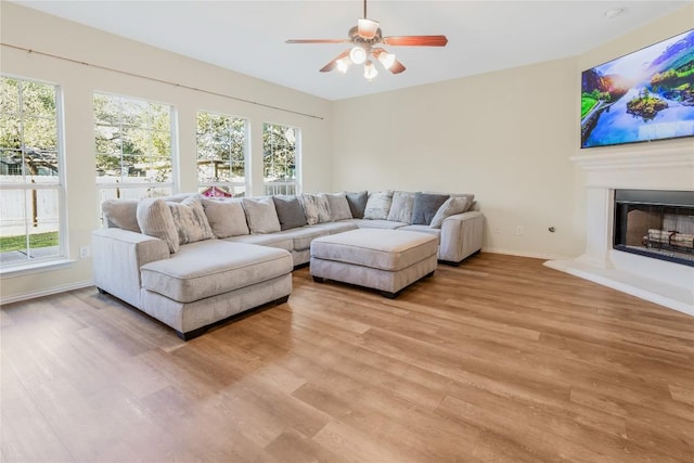 living room with light wood finished floors, ceiling fan, plenty of natural light, and baseboards