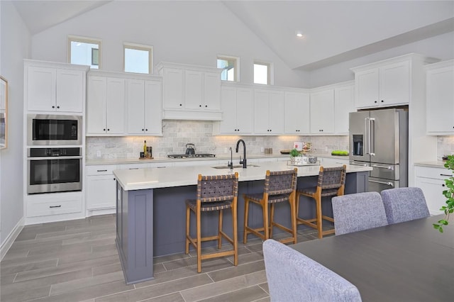6108 Antelope Well Ln, Austin, TX 78738 - kitchen featuring appliances with stainless steel finishes, high vaulted ceiling, a sink, a breakfast bar, and white cabinets