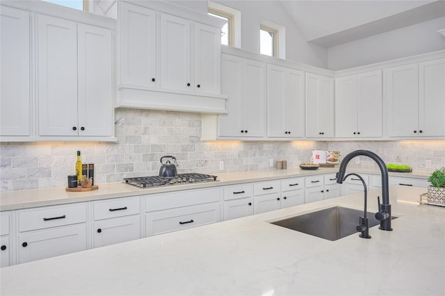 6108 Antelope Well Ln, Austin, TX 78738 - kitchen with stainless steel gas cooktop, a sink, white cabinets, decorative backsplash, and vaulted ceiling