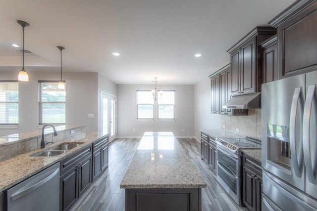 121 Grassy Ln, Elgin, TX 78621 - kitchen with appliances with stainless steel finishes, under cabinet range hood, a kitchen island, wood finished floors, and backsplash