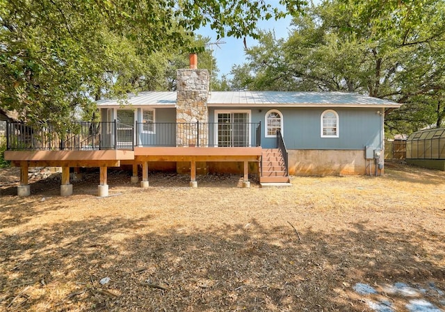back of house featuring metal roof, a wooden deck, a chimney, an exterior structure, and stairway