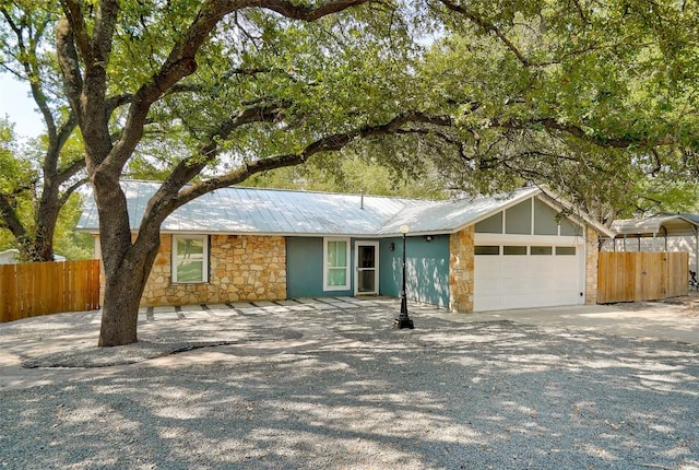 single story home with stone siding, fence, an attached garage, driveway, and metal roof