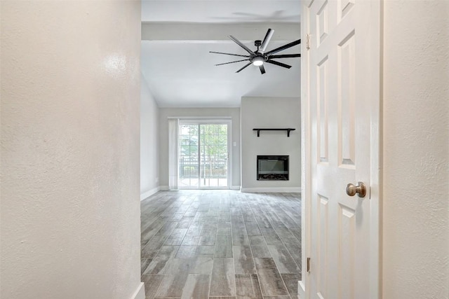 unfurnished living room with baseboards, wood finished floors, a ceiling fan, a glass covered fireplace, and lofted ceiling