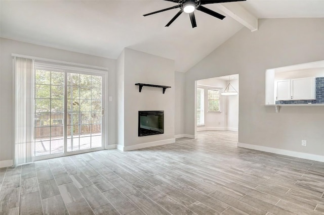 unfurnished living room featuring ceiling fan, beamed ceiling, light wood-type flooring, baseboards, and a glass covered fireplace