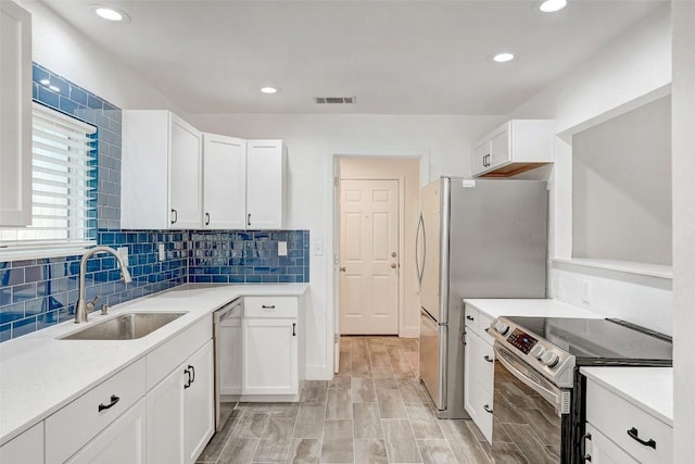 kitchen featuring stainless steel appliances, a sink, white cabinets, tasteful backsplash, and light countertops