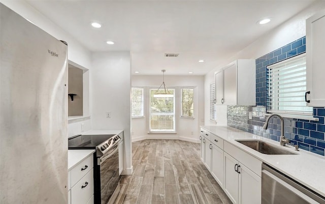 kitchen with appliances with stainless steel finishes, a sink, white cabinetry, light wood-style floors, and tasteful backsplash