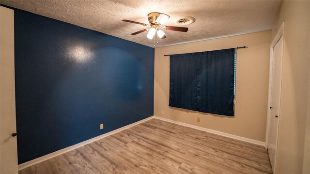 empty room with a textured ceiling, ceiling fan, wood finished floors, and baseboards
