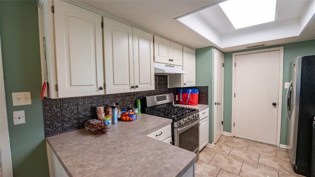kitchen with appliances with stainless steel finishes, under cabinet range hood, decorative backsplash, light countertops, and baseboards