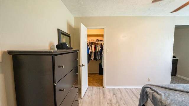 bedroom featuring a spacious closet, light wood-type flooring, a textured ceiling, baseboards, and a closet