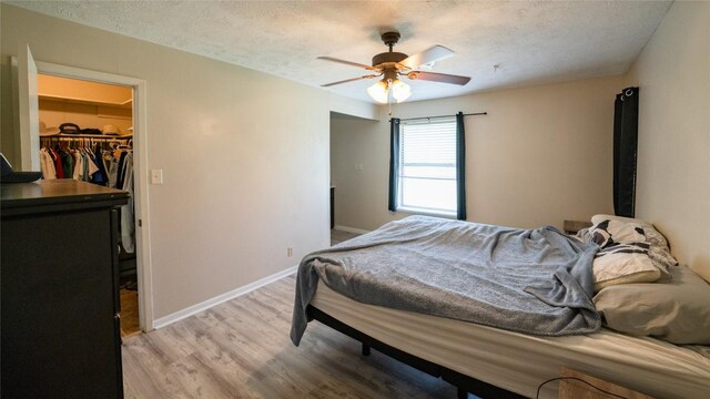 bedroom featuring a spacious closet, light wood-style floors, baseboards, a textured ceiling, and a closet