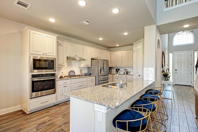 1816 Ficuzza Way, Leander, TX 78641 - kitchen featuring appliances with stainless steel finishes, light wood-style floors, light stone countertops, under cabinet range hood, and a kitchen breakfast bar