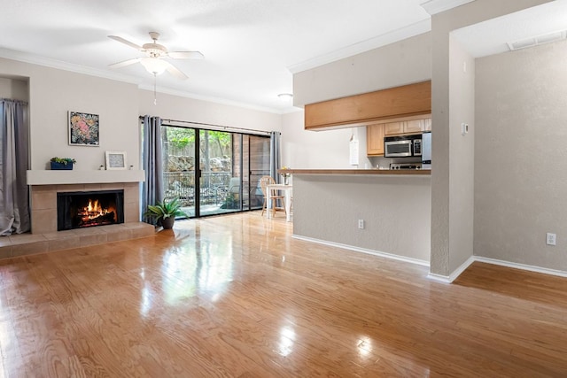 unfurnished living room with baseboards, light wood-style flooring, ceiling fan, ornamental molding, and a fireplace