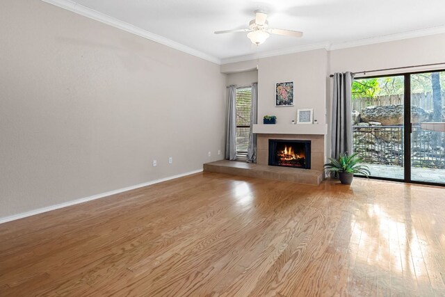 unfurnished living room featuring wood finished floors, a fireplace, ceiling fan, crown molding, and baseboards