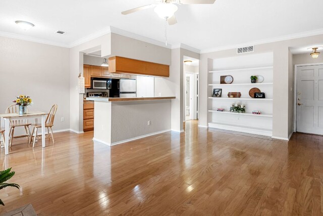 living room featuring built in shelves, ceiling fan, light wood-type flooring, crown molding, and baseboards