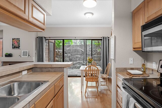 kitchen with electric stove, stainless steel microwave, tile counters, light wood-style flooring, and ornamental molding