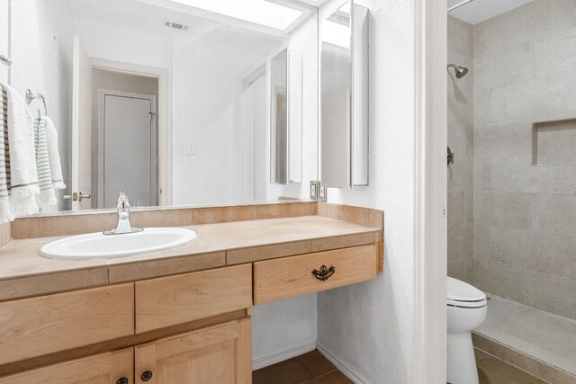 bathroom featuring a tile shower, toilet, vanity, and tile patterned flooring