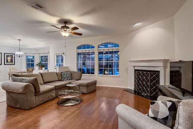 living room with a chandelier, a fireplace with raised hearth, wood finished floors, and ceiling fan