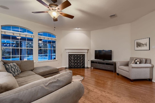 living area featuring ceiling fan, wood finished floors, a fireplace with flush hearth, and baseboards