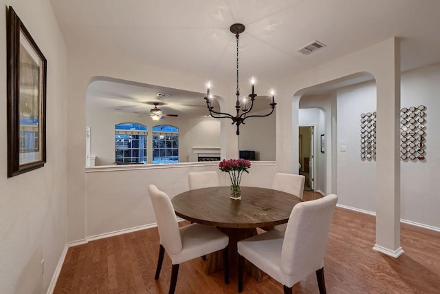 dining room featuring arched walkways, ceiling fan, wood finished floors, a chandelier, and baseboards