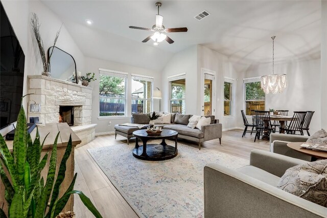 living area featuring plenty of natural light, a stone fireplace, a chandelier, lofted ceiling, and light wood-style floors